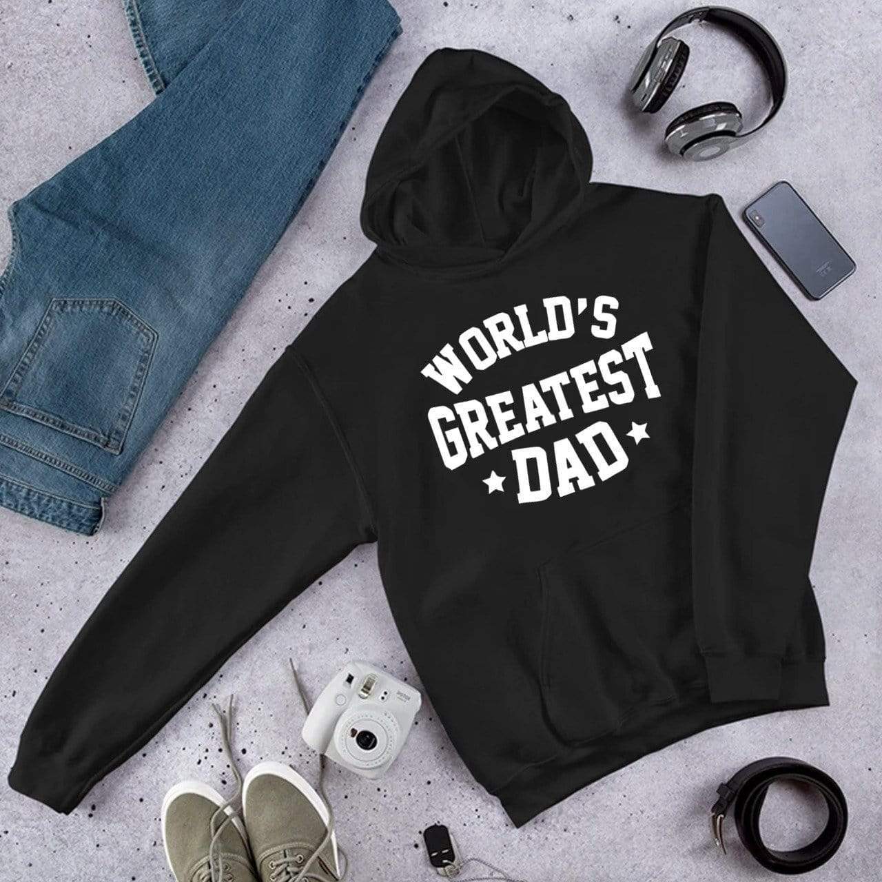 A black hoodie with 'WORLD'S GREATEST DAD' printed in white text on the front, displayed alongside casual clothing and accessories.